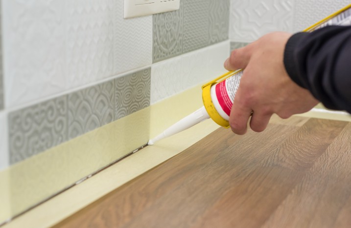 Arbeiter füllt die Naht zwischen den Keramikfliesen an der Wand und der Küchenarbeitsplatte