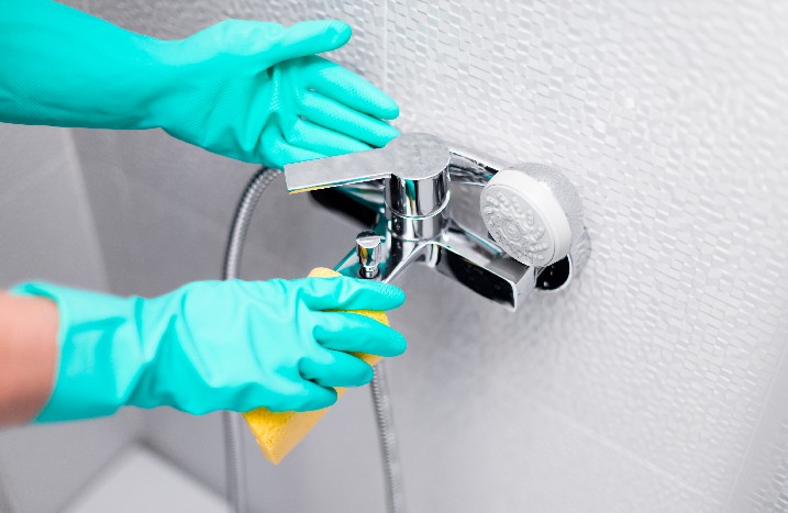 Person mit Handschuhen reinigt eine Duscharmatur.