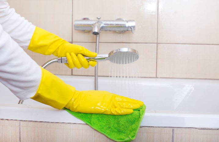Eine Person mit gelben Handschuhen reinigt die Duschwanne.