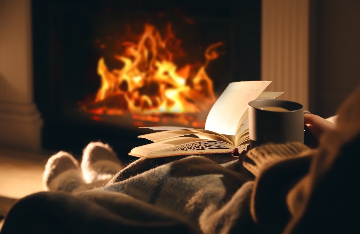 Frau relaxt mit Buch und Tee vor dem Kaminfeuer