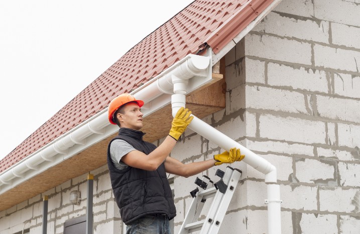 Handwerker bringt Fallrohr an Dachrinne an