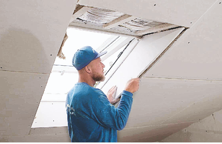 Ein Handwerker verkleidet die Seiten eines Dachfensters mit Gipskarton.
