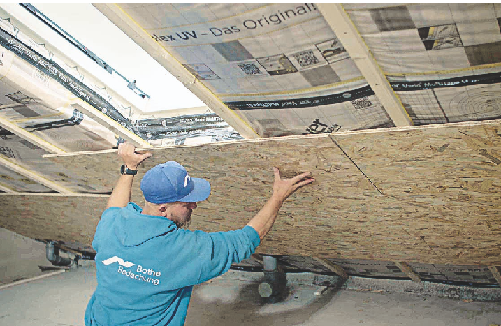 Ein Handwerker hält OSB-Platten an die Dachschräge, um die Dachschräge damit zu verkleiden.