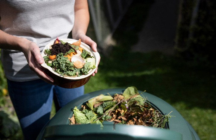 Frau füllt Schüssel mit neuen Kompost in die Tonne