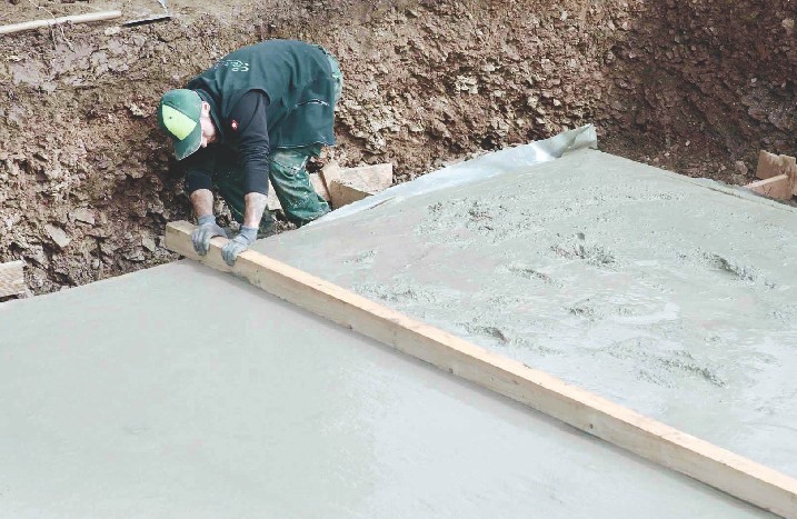 Ein Mann streicht Beton mit einem Kantholz glatt.