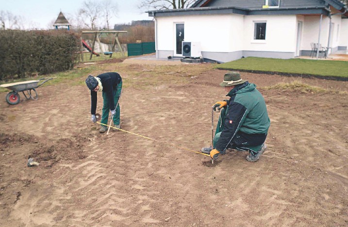 Zwei Männer messen in einem Garten die Fläche für ein Pool-Fundament aus.