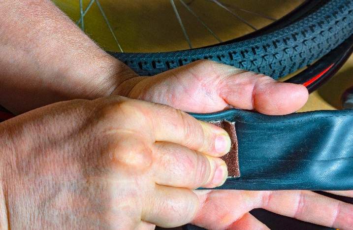 Ein Mann raut die Oberfläche eines Fahrradschlauchs mit Schleifpapier an.