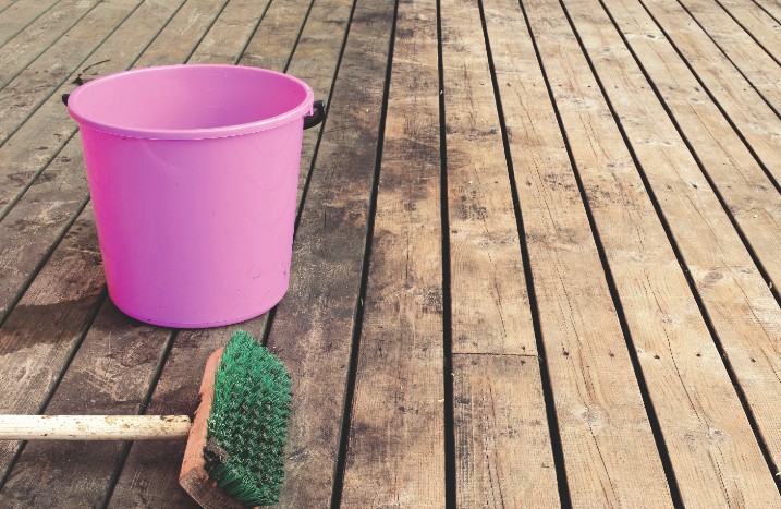Ein pinker Eimer und eine Bürste auf einer Holzterrasse.