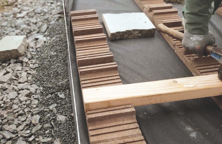In ein Streifenfundament wird der erste Holzbalken eingeklopft.