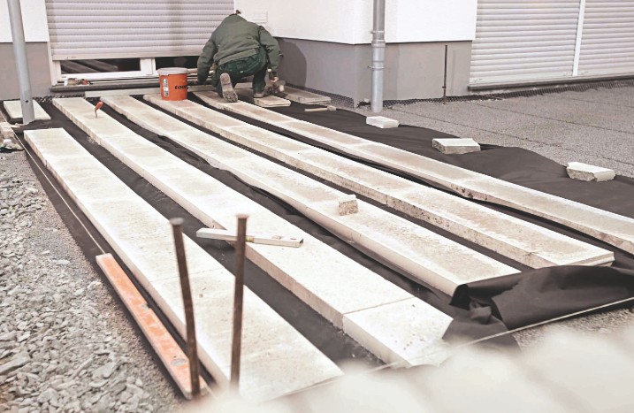 Als Unterbau für eine Holzterrasse werden vier Bahnen Betonplatten verlegt.