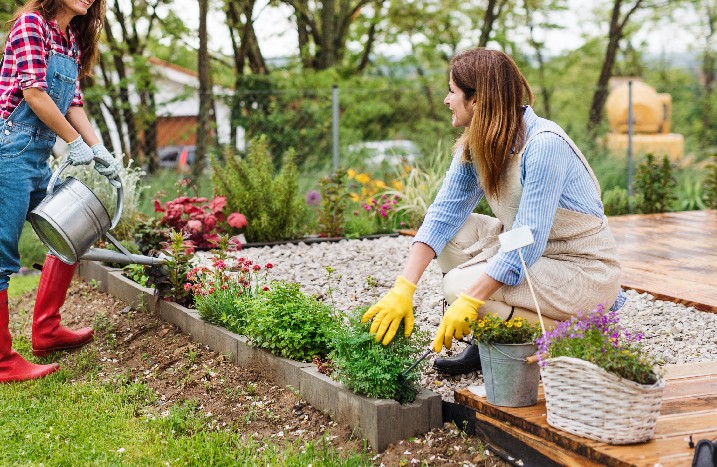 Zwei Frauen bepflanzen Blumenbeet neben einer Terrasse