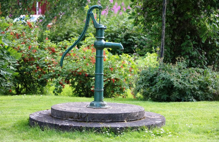 Brunnenpumpe auf Steinplatte in einem Garten.