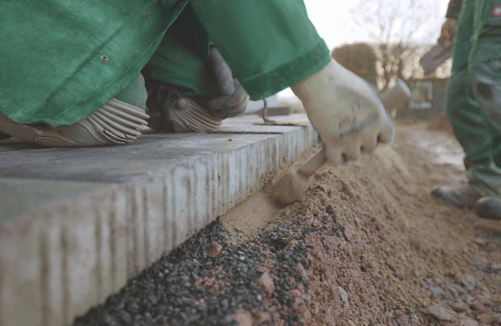 Ein Handwerker stampft Beton unter Pflastersteine.