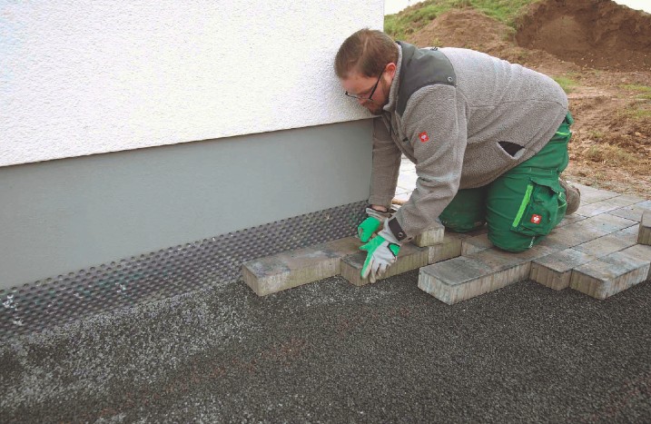 Ein Handwerker verlegt Pflastersteine an einer Hauswand.