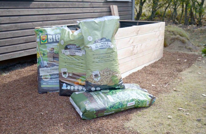 Vier Säcke Erde und Mulch vor einem selbstgebauten Hochbeet.
