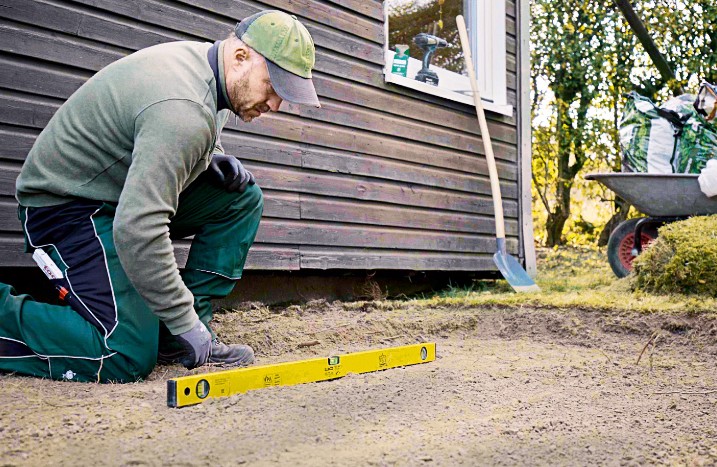 Ein Handwerker misst den Gartenboden mit einer Wasserwaage aus.
