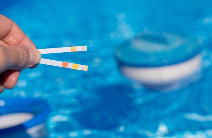 Eine männliche Hand hält zwei Prüfstreifen für die Wasserqualität eines Pools.