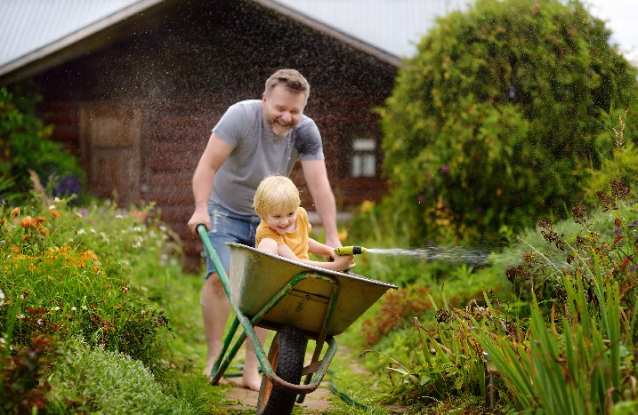 Kind setz in Schubkarren und netzt den Garten mit einem Gartenschlauch