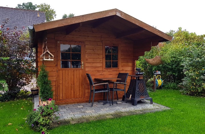 Gartenhaus mit Fenster und Vordach auf einer Wiese.