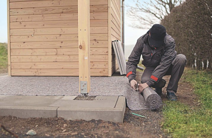 Ein Mann legt Malervlies um ein Gartenhaus herum.