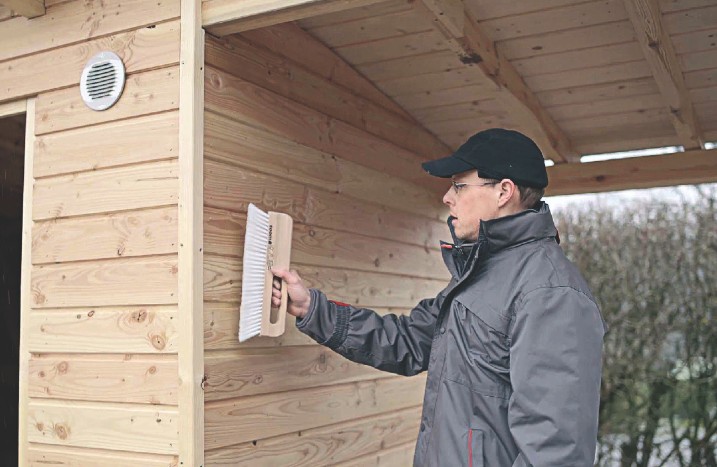 Ein Mann reinigt ein Gartenhaus mit einer Bürste.