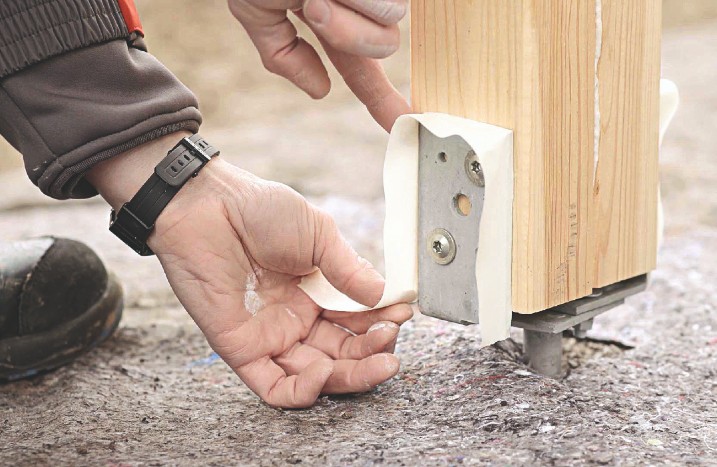 Jemand klebt die Ränder eines Holzpfostens ab.