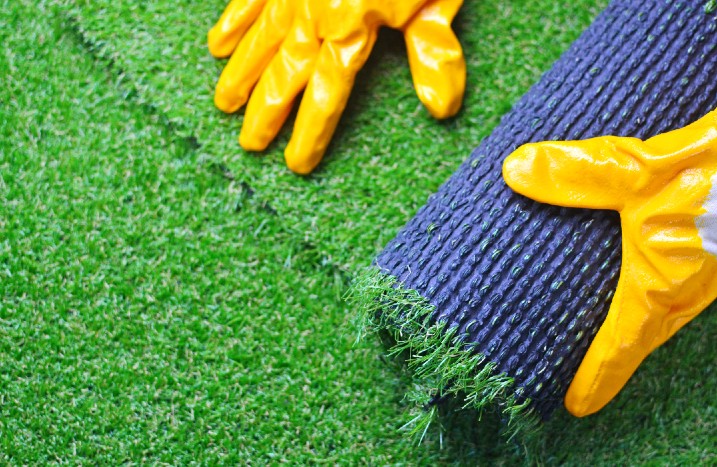 Kunstrasen wird ausgerollt mit Handschuhen