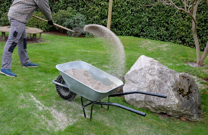 Mann streut mit Schaufel Sand auf den Rasen