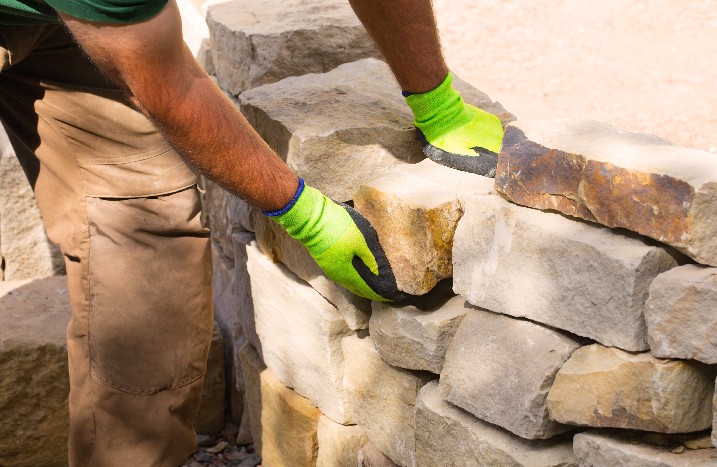 Ein Mann mit Handschuhen baut Trockenmauer im Garten