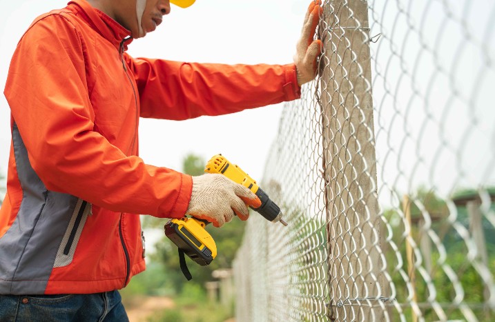 Ein Handwerker montiert einen Maschendrahtzaun.