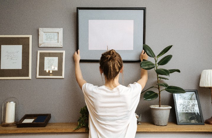 Eine Frau richtet einen Bilderrahmen an der Wand aus.