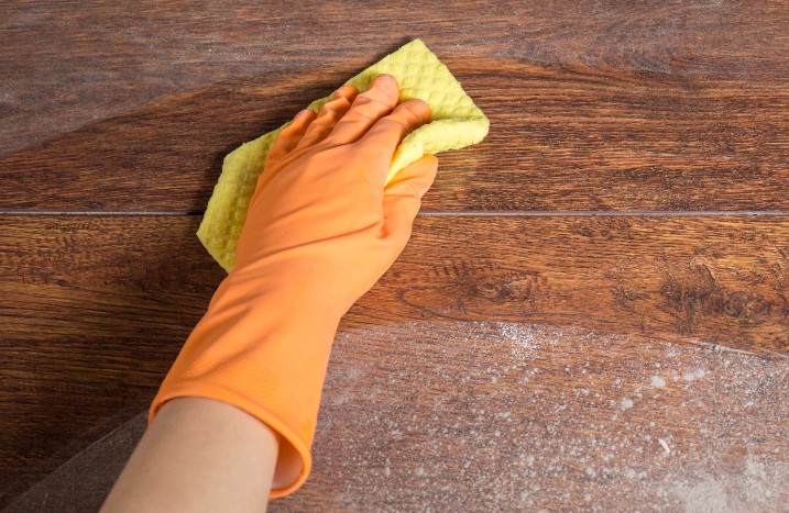 Hand mit Handschuh und Schwamm reinigt Laminat