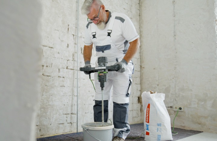 Ein Handwerker rührt Putz mit einem elektrischen Rührquirl an.