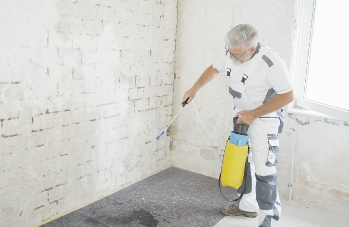 Ein Handwerker sprüht Grundierung an eine weiße Ziegelwand.