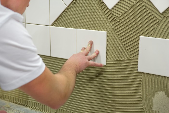 Mann legt fliesen auf Wand