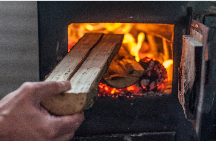 Mann legt Brennholz in Kaminofen nach.