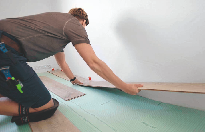 Handwerkerin verlegt die erste Reihe Laminatboden.
