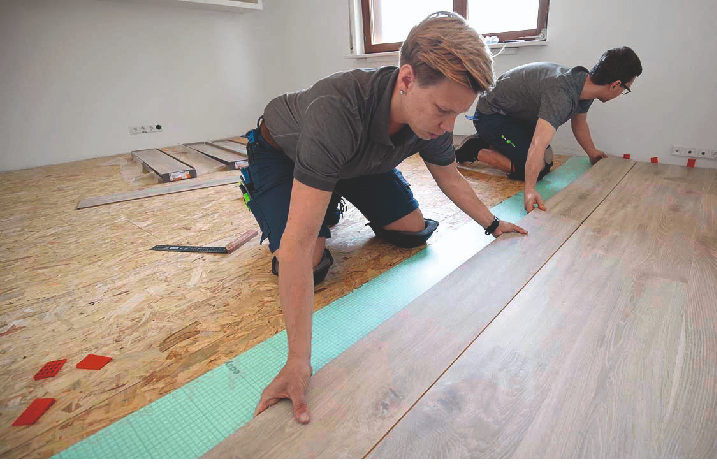 Zwei Handwerker verlegen gemeinsam eine Reihe Laminat.