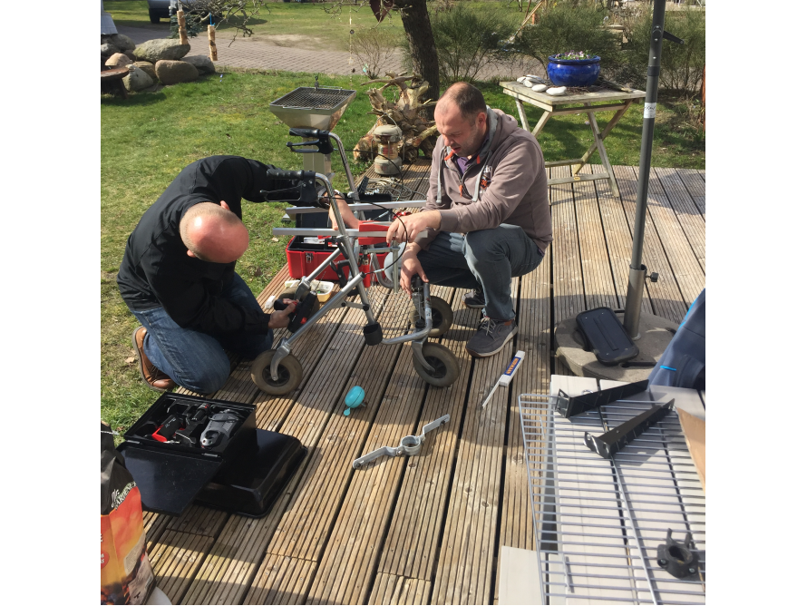Zwei Personen reparieren eine Gehhilfe mit Werkzeug auf einer Holzterrasse