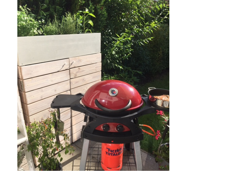 Roter Gasgrill auf Terrasse vor Gartenhaus