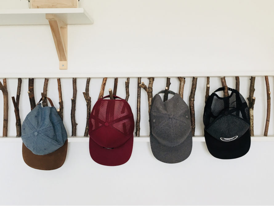 Vier Baseballmützen an einem Garderobenständer aus Ästen