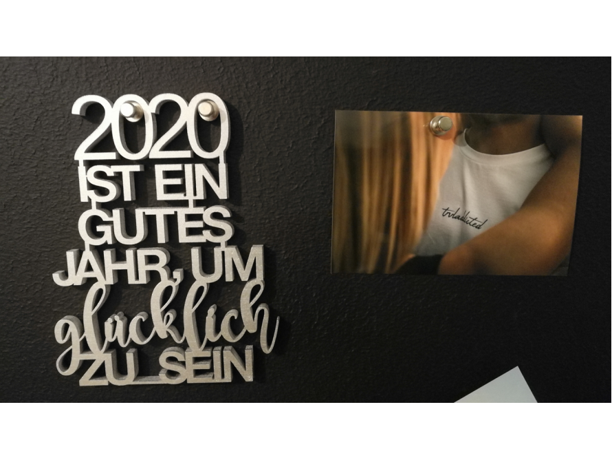 Silberner Schriftzug "2020 ist ein gutes Jahr, um glücklich zu sein" und Foto einer Umarmung an schwarzer Pinnwand
