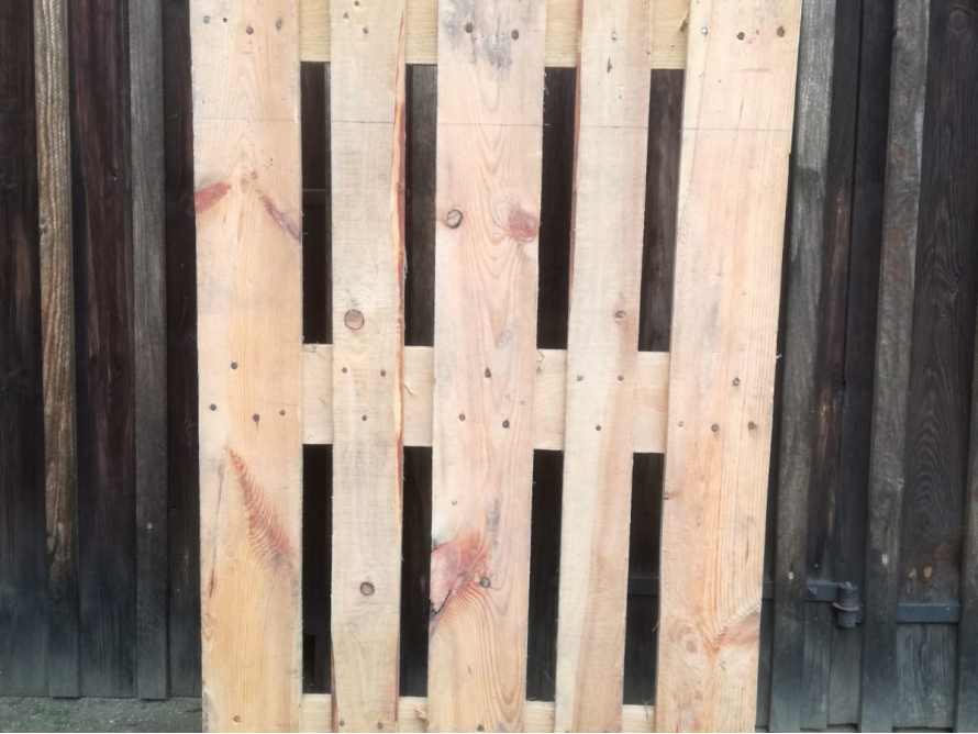 Eine Holzpalette lehnt an einer Holzwand.