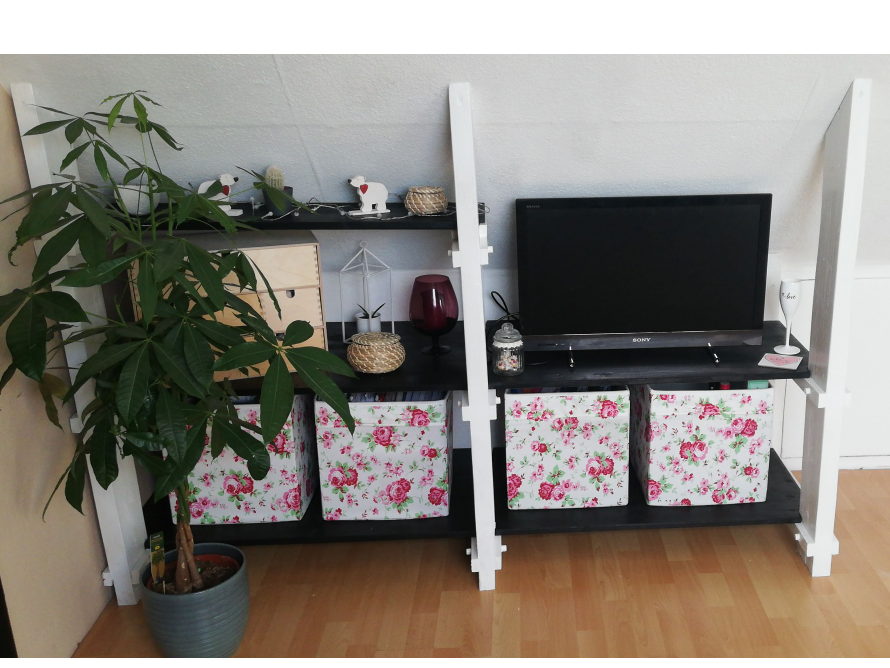 Ein weißes Regal mit einem Fernseher und Aufbewahrungsboxen.