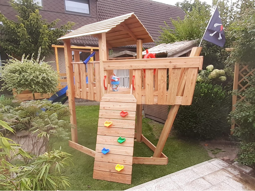 Hölzernes Spielgerät in Form eines Piratenschiffs mit Rutsche und Kletterwand.