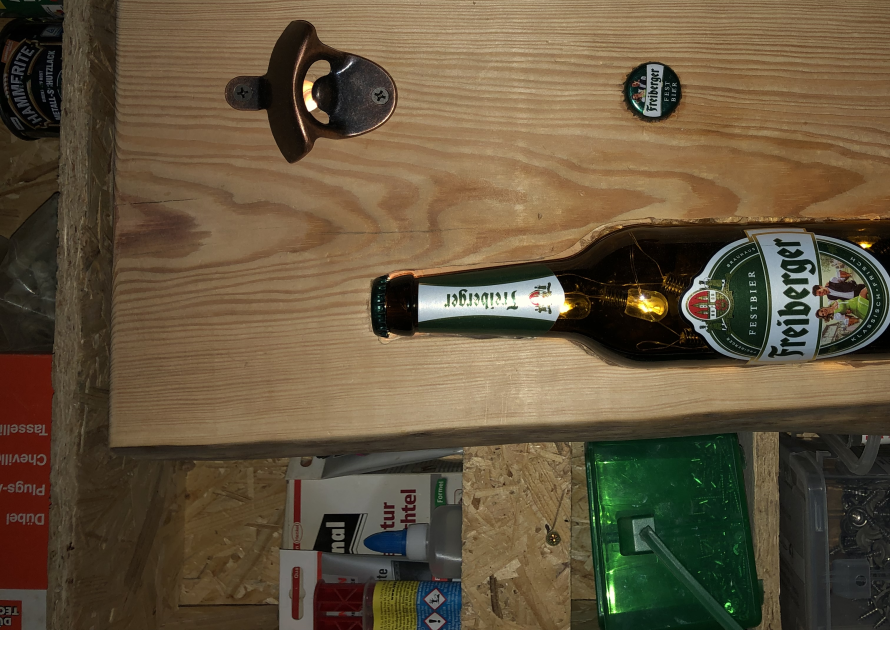 Ein Flaschenöffner und eine leere Glasflasche in einem Holzbrett.