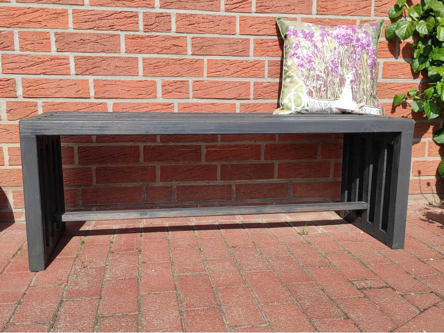 Schwarze Holzbank vor Backsteinmauer