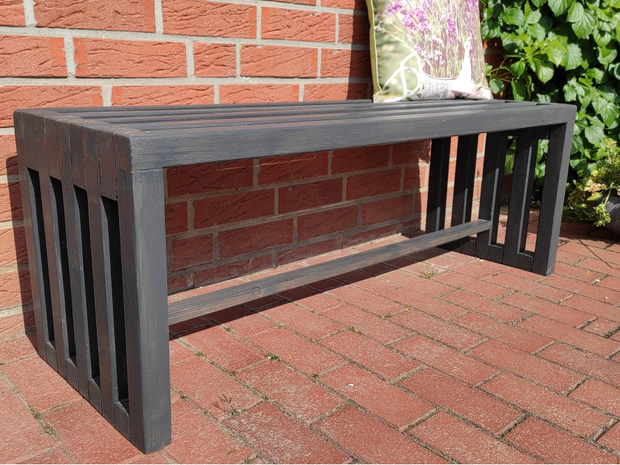 Schwarze Holzbank an einer Backsteinmauer