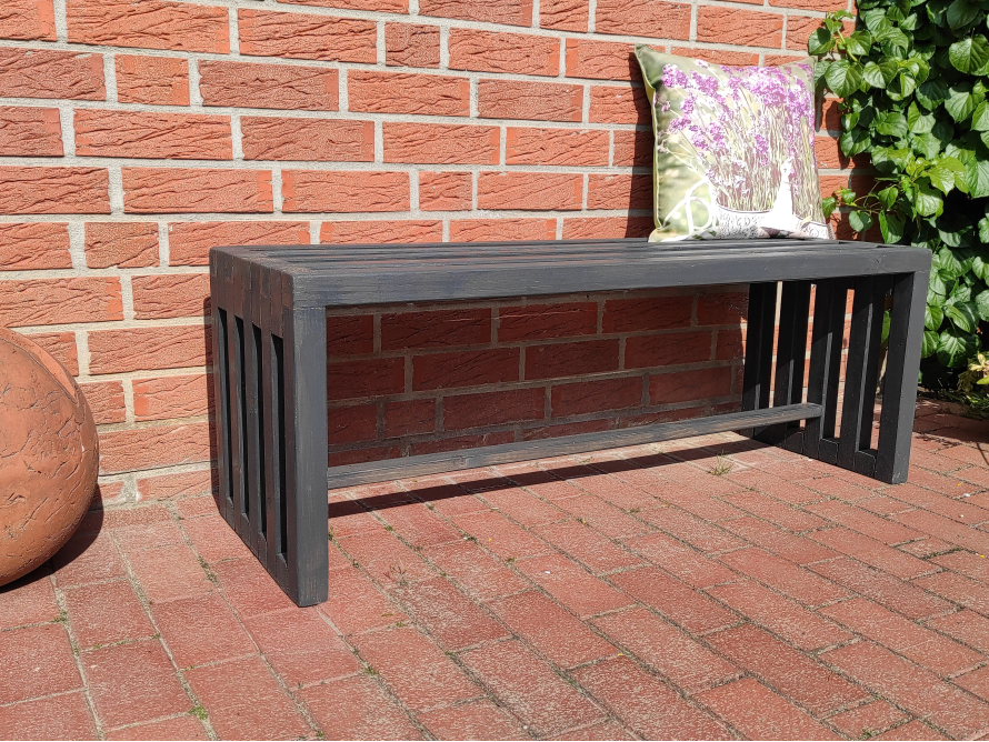 Schwarze Holzbank an einer Backsteinwand