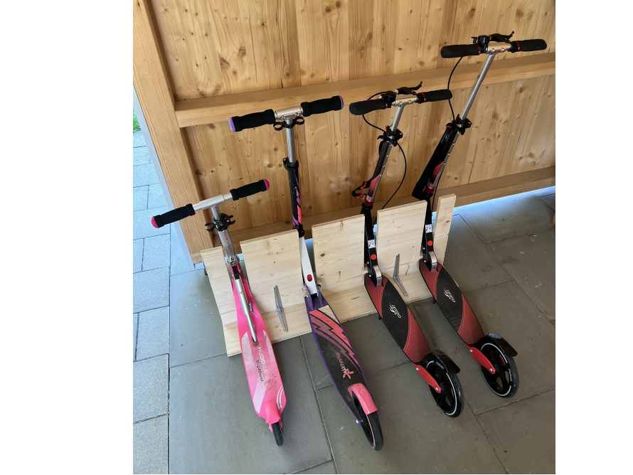 Vier Tretroller stehen an einer Holzkonstruktion